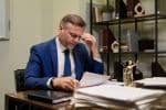 Middle Aged Caucasian Man Reading Documents and Thinking at Office Desk